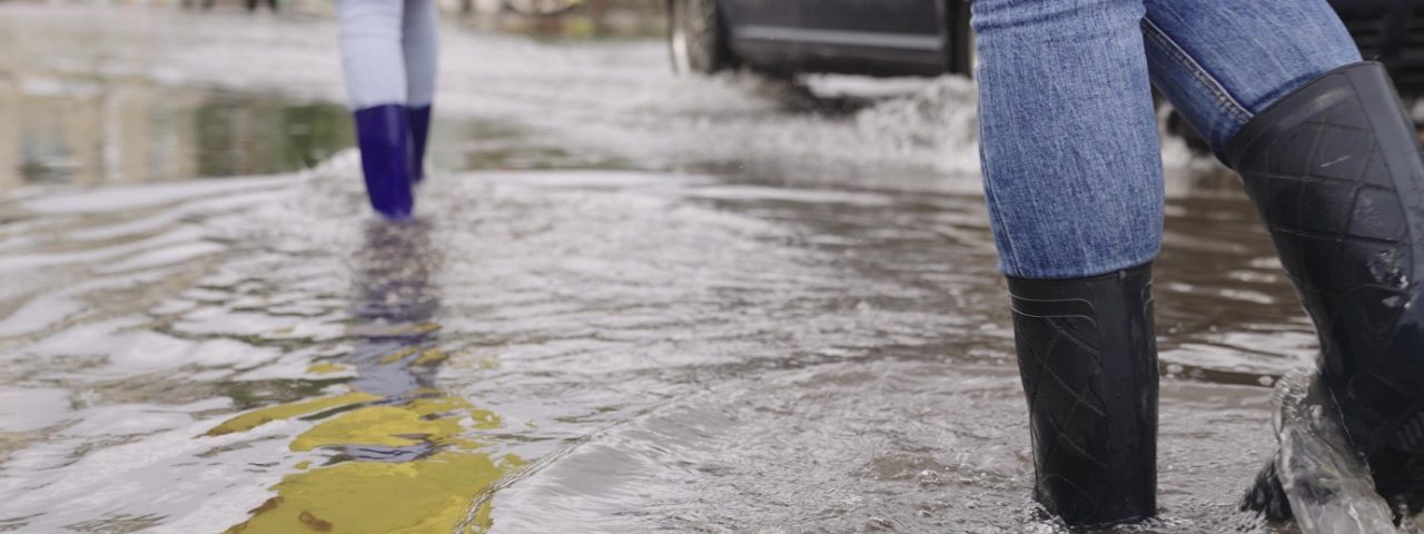 Girls,In,Raincoats,And,Rubber,Boots,Walk,Along,Road,Flooded